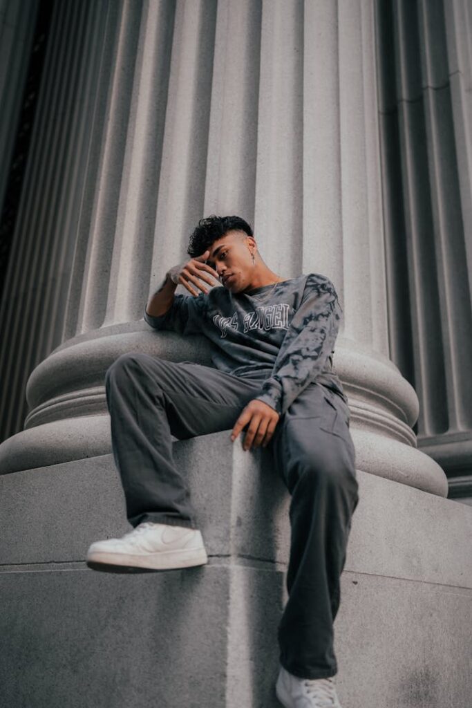 Stylish man in casual wear posing by a city column, showcasing urban fashion.