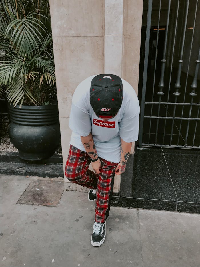 A fashionable tattooed man in a casual outfit standing outdoors, leaning forward with urban vibes.