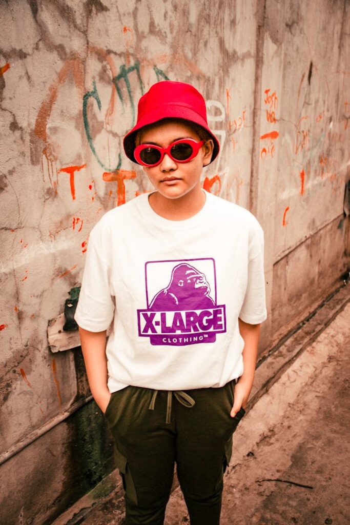 Stylish individual in streetwear, featuring a bold red hat and sunglasses against a graffiti backdrop.