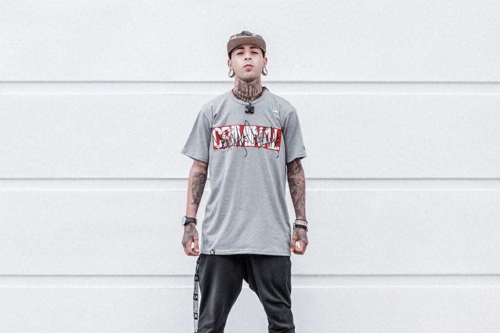 Portrait of a fashionable tattooed young man wearing streetwear against a minimalist background.