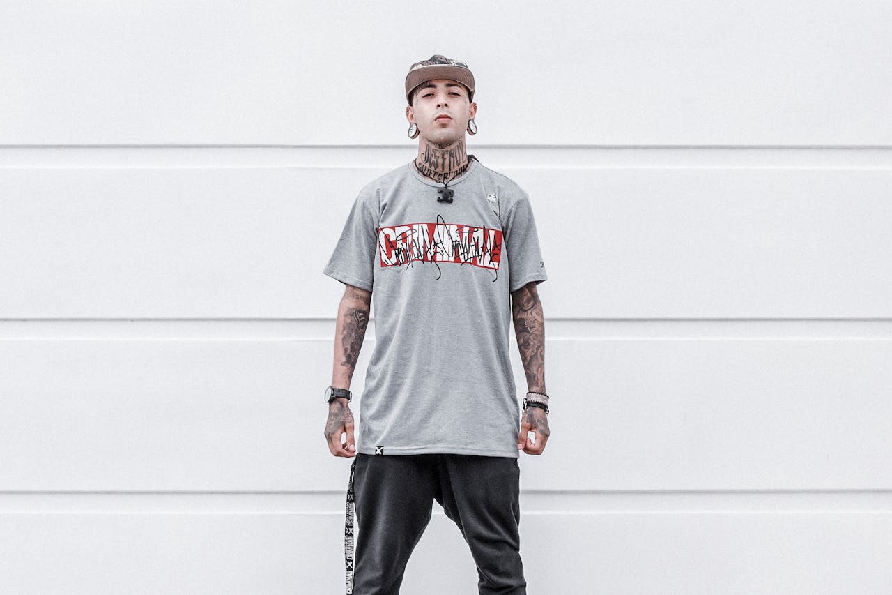 Portrait of a fashionable tattooed young man wearing streetwear against a minimalist background.